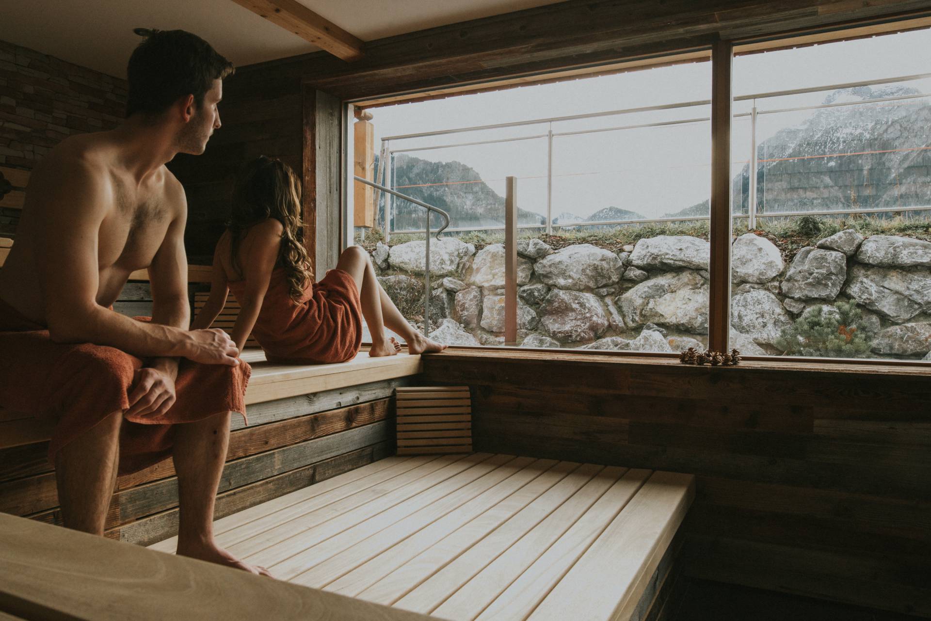 Personen sitzen in Panoramasauna mit Bergblick