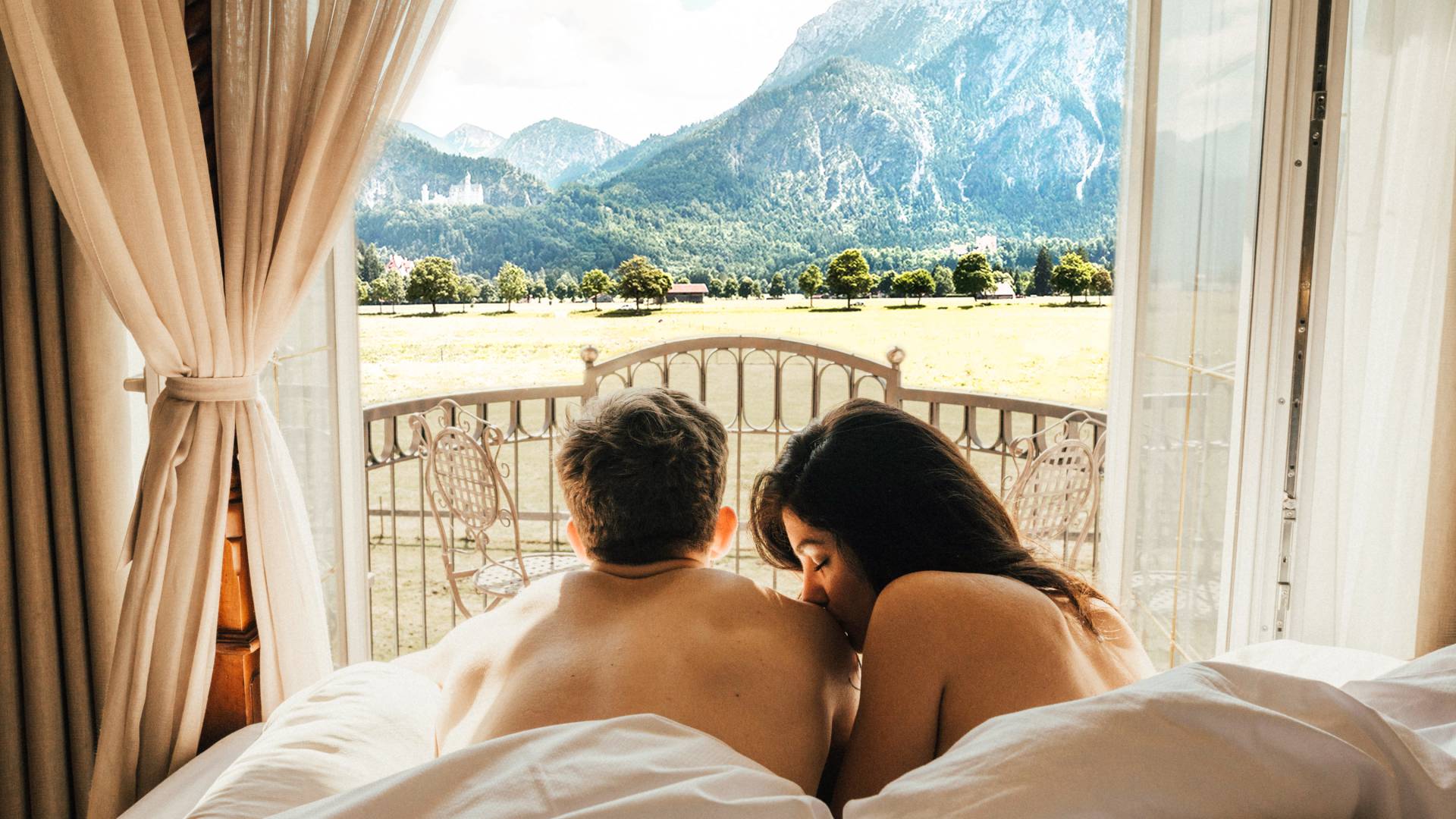 Pärchen genießt die Aussicht auf Schloss Neuschwanstein vom Hotelbett aus