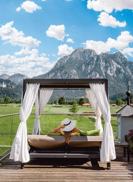 Wellnessurlaub im Allgäu - Frau in Dailybett entspannt mit Blick auf das Schloss und die Berge