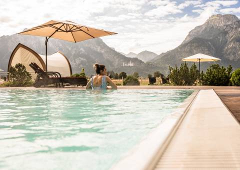 Wellnesshotel Schwangau - Person genießt die Aussicht vom Außenpool auf die Berge